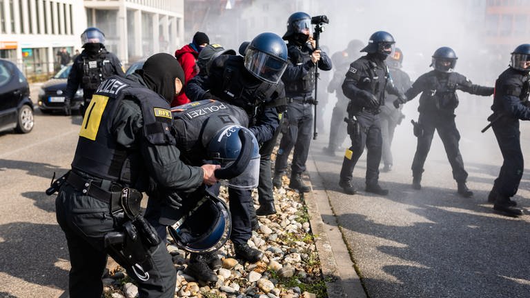 Ein von einem Pulverlöscher getroffener Polizist wird während einer Demonstration gegen den Landesparteitag der AfD Baden-Württemberg von zwei weiteren Polizisten versorgt.