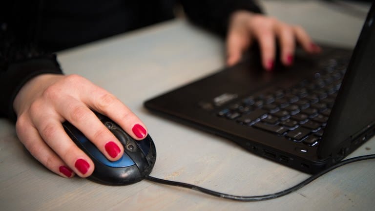 Eine Frau sitzt an einem Laptop und bedient eine Maus.