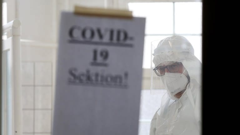 Johannes Manhart, Facharzt für Rechtsmedizin, steht hinter einer Tür im Sektionssaal der Universitätsmedizin, an der ein Zettel mit der Aufschrift "COVID-19 Sektion!" befestigt ist. Hier werden an Covid-19 Verstorbene obduziert, um die konkrete Todesursache festzustellen. 
