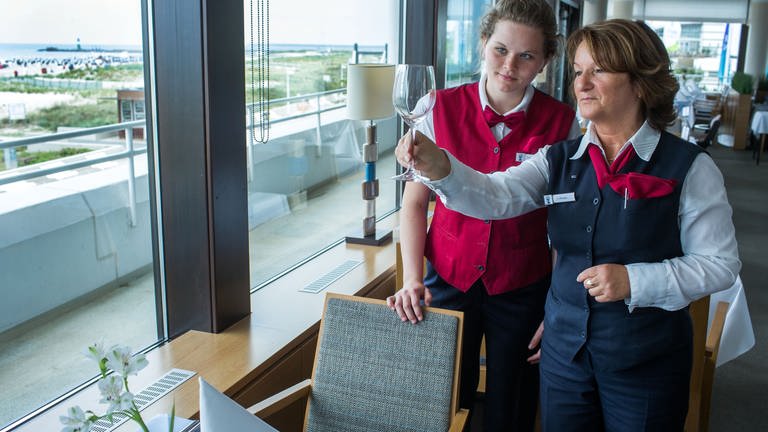 Eine Schülerpraktikantin aus der zehnten Klasse deckt in einem Hotel mit einer Restaurantfachfrau einen Tisch ein.