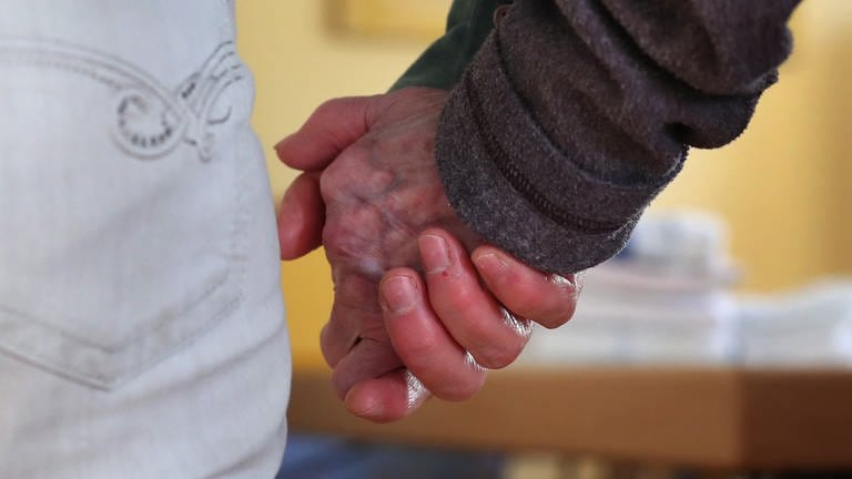 Eine Pflegekraft hält die Hand eines alten Menschen. 