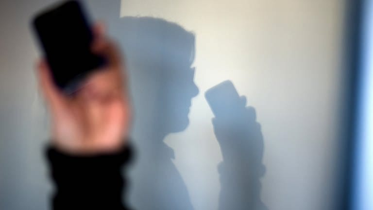 Eine Frau telefoniert mit ihrem Mobiltelefon - an der Wand zeichnet sich ihr Schatten ab. 