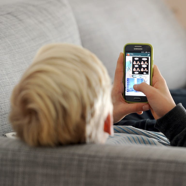 Ein Jugendlicher liegt auf einem Sofa und schaut auf sein Smartphone.