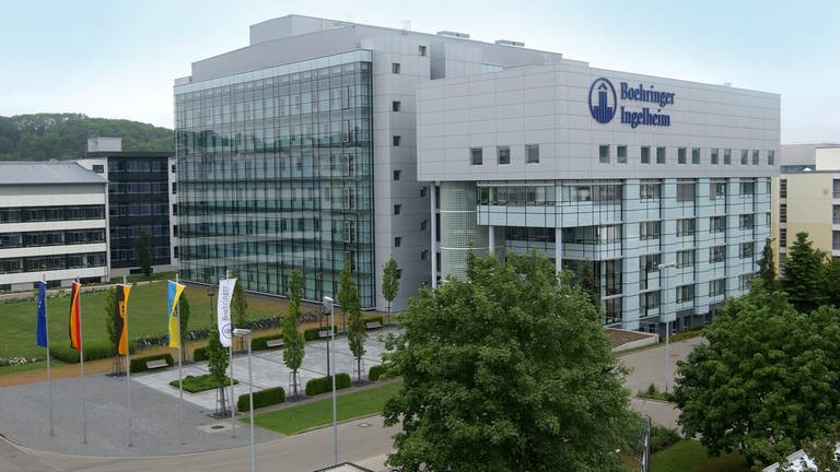 Firmengebäude des Pharmakonzerns Boehringer Ingelheim für die Biopharmazie in Biberach aus Glas und grauem Beton. Auf der Vorderseite des Gebäudes steht in großen, blauen Buchstaben der Firmenname.