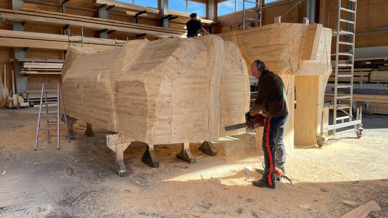 Ein Mann arbeitet mit der Motorsäge an einer Holzkuh. (Foto: SWR)