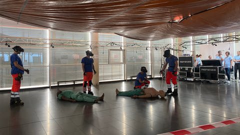 Vier Mediziner des Uniklinikums Heidelberg trainieren den Ernstfall. Zwei verletzte Puppen liegen auf den Boden. 18 weitere Verletzte sind digital über die VR-Brillen zu sehen.