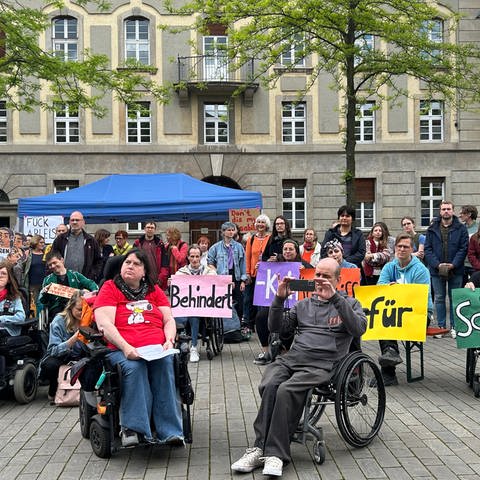Menschen mit Rollstühlen und ohne haben sich in Heidelberg versammelt. Sie halten Banner und protestieren für mehr Inklusion. (Foto: SWR)