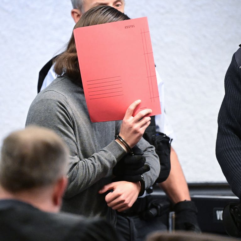 Ein Angeklagter hält sich im Januar 2024 beim Auftakt des Prozesses einen Ordner vor sein Gesicht. (Foto: dpa Bildfunk, picture alliance/dpa | Bernd Weißbrod)