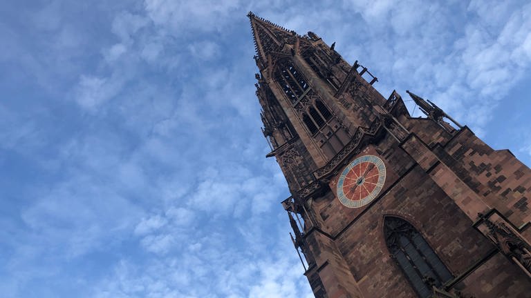 Das Freiburger Münster ist von schräg unten zu sehen. Der Turm ragt nach oben. Der Himmel ist blau
