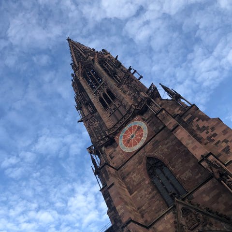 Das Freiburger Münster ist von schräg unten zu sehen. Der Turm ragt nach oben. Der Himmel ist blau