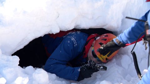 Ein Mann ist zu Übungszwecken für Lawinenhunde im Schnee vergraben