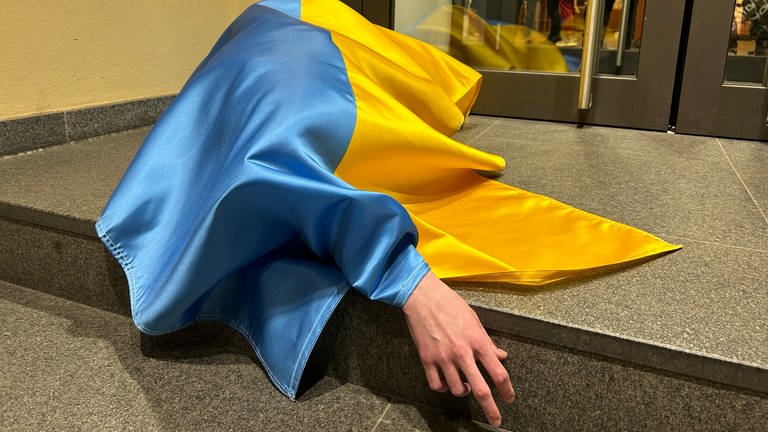 Eine ukrainische Flagge bedeckt einen Menschen am Boden. (Foto: SWR, Louise Schöneshofer)