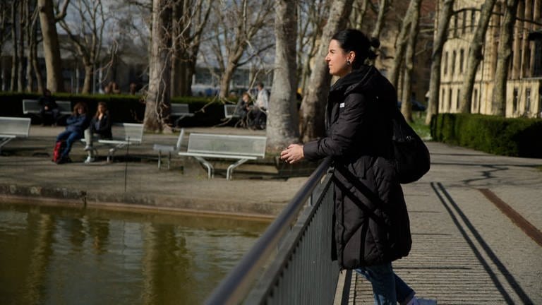 Sina Frehner steht auf einer Brücke auf dem Gelände der Uniklinik Freiburg und schaut nachdenklich in den Teich vor ihr.  (Foto: SWR)