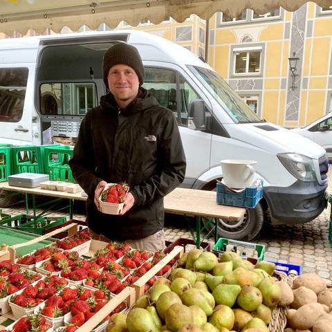 Obstbauer David Sexauer an seinem Stand auf dem Freiburger Münstermarkt mit einer Schale Erdbeeren in der Hand