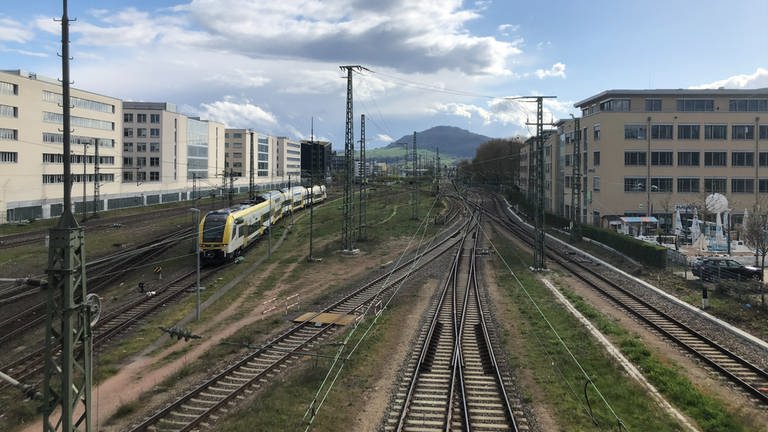Blick auf den Schönberg, im Vordergrund liegen viele Zuggleise. Auf einem fährt ein gelber Zug, der Breisgau-S-Bahn. (Foto: SWR, Paula Zeiler)