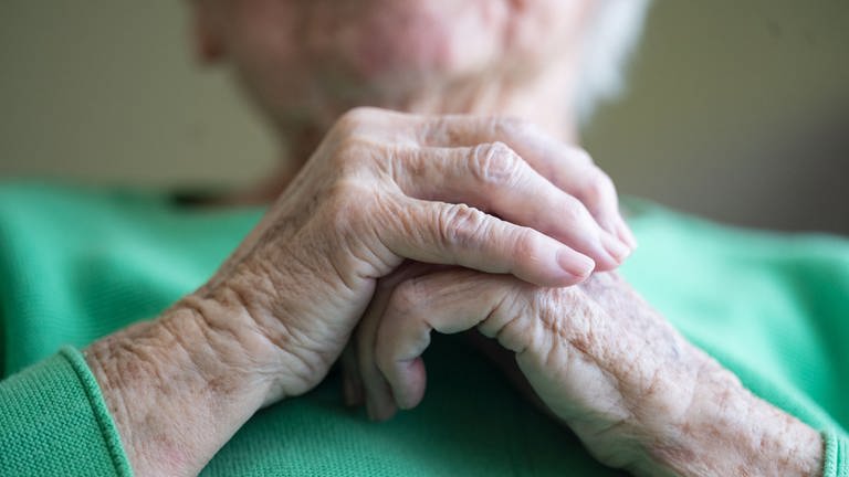 Eine Bewohnerin eines Seniorenhaus faltet ihre Hände. In der Pflegeeinrichtung "Haus am Neckar" saßen die Bewohnerinnen und Bewohner des Erdgeschosses fast eine Woche hinter verschlossenen Rolläden. 