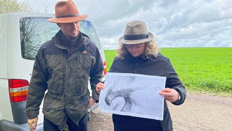 Zwei Menschen mit Hüten vor einer grünen Wiese in der Nähe von Bad Niedernau mit einer Schwarzweiß-Karte, auf der sich Gekände-Formationen erkennen lassen.  (Foto: SWR, Peter Binder)