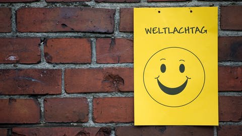 Smileyposter an Mauer mit Schriftzug Weltlachtag: Der Weltlachtag ist immer am ersten Sonntag im Mai. Was gibt es für verschiedene Lachtypen?
