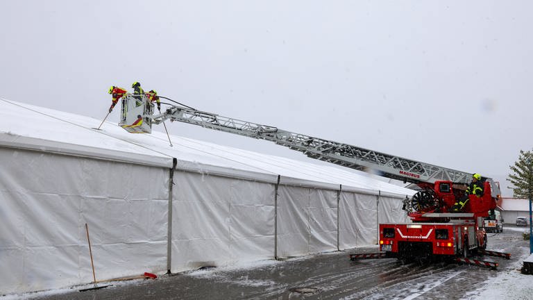 Feuerwehrleute stehen im Korb einer Drehleiter über dem Dach des Festzeltes in Riedlingen-Zell (Kreis Biberach).  Sie kehren Schnee vom Zelt.  (Foto: Thomas Warnack)