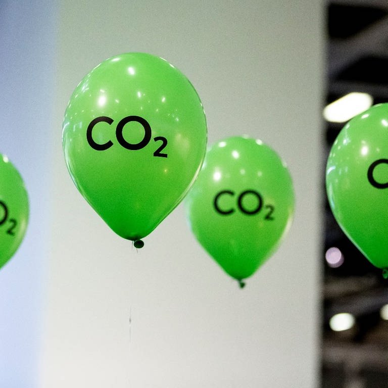Grüne Luftballons mit der Aufschrift "CO2" schweben an einem Messesstand. (Foto: dpa Bildfunk, picture alliance/dpa | Christoph Soeder)