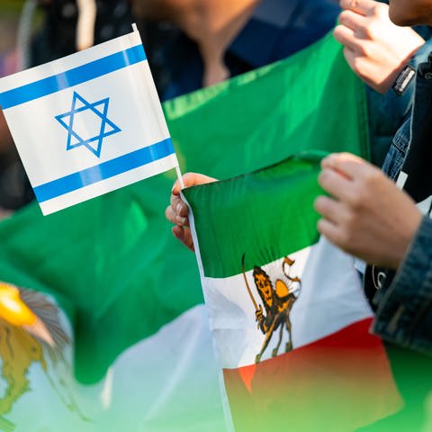 Eine Frau hält eine israelische und eine iranische Fahne während einer Kundgebung auf der Wiese gegenüber des iranischen Konsulats in Hamburg. (Foto: dpa Bildfunk, picture alliance/dpa | Jonas Walzberg)