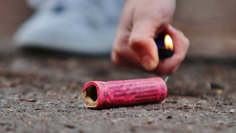 Ein Feuerzeug in der Hand eines Jugendlichen zündet einen Böller auf der Straße (Foto: IMAGO, IMAGO Bildnummer: 0109254911)