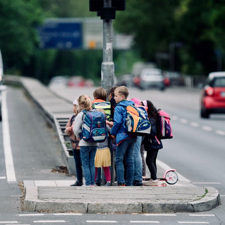 Eine Schülergruppe testet einen eventuellen, künftigen Schulweg und steht auf einer Verkehrsinsel inmitten einer viel befahrenen Straße.