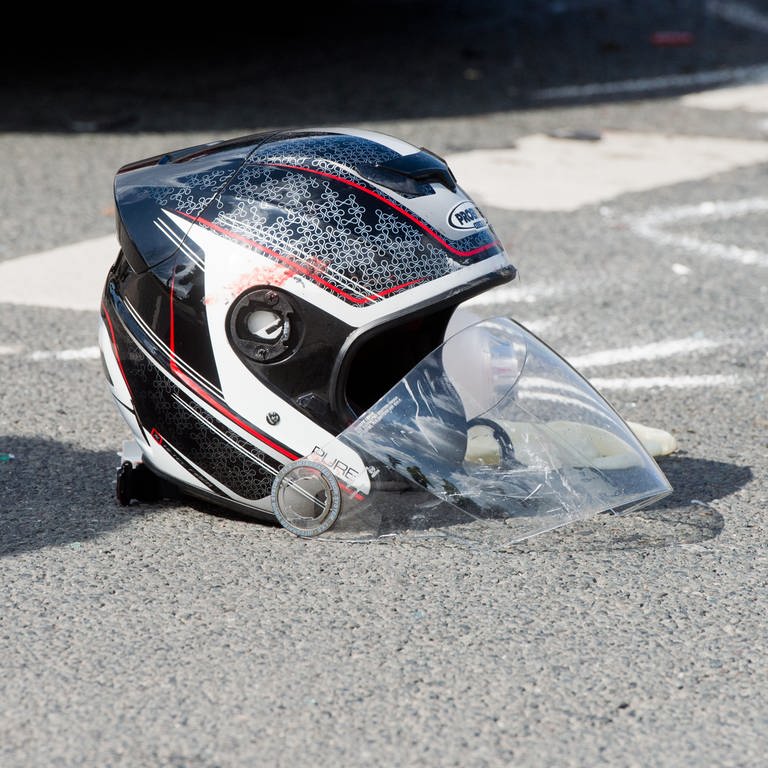 Ein beschädigter Helm liegt nach einem schweren Motorradunfall auf einer Straße 