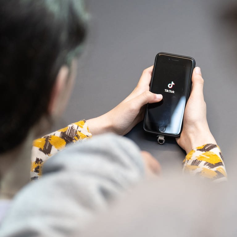 Eine Jugendliche schaut auf ein Handy mit TikTok-Logo - nach einer TikTok-Challenge ist eine Schülerin aus Kaiserslautern ins Krankenhaus gekommen. (Foto: dpa Bildfunk, picture alliance/dpa | Hannes P. Albert)