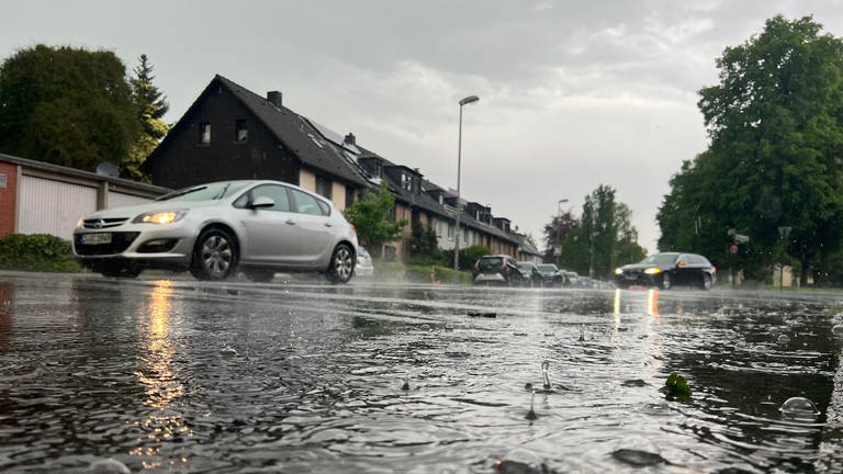 Autos fahren bei einem Gewitter eine teilweise überflutete Straße entlang. Der Deutsche Wetterdienst warnt vor Überflutungen. Es gilt teils die höchste Warnstufe in Rheinland-Pfalz.