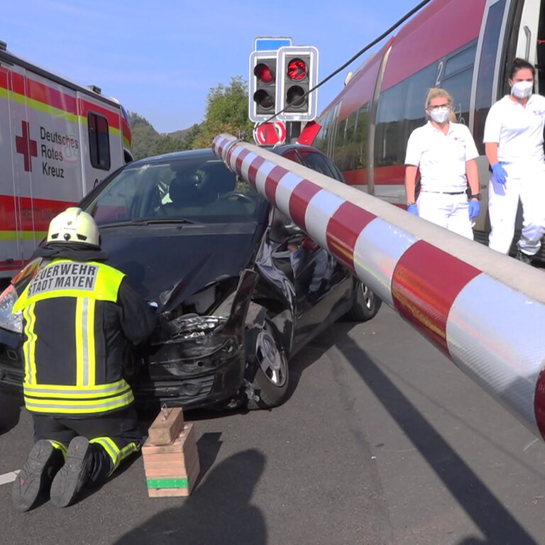 Unfall am beschrankten Bahnübergang: Ein Rettungswagen und Helfer an einem Pkw, die Schranke ist geschlossen und ein Zug steht