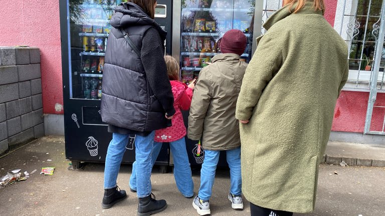 Menschen stehen vor einem Automatenkiosk in Polch und suchen sich Waren aus