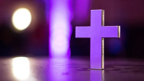 Ein weißes Kreuz schimmert in lilafarbenem Licht.