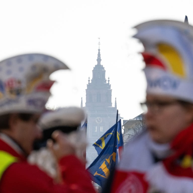 Mitglieder des Mainzer Carneval-Vereins stehen kurz vor Beginn des Rosenmontagsumzuges 2023 in Mainz in der Flucht mit dem Turm des Doms.
