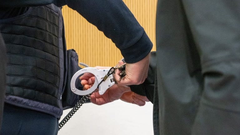 Justizbediensteter entfernt Handfessel des Angeklagten im Trierer Amokprozess.