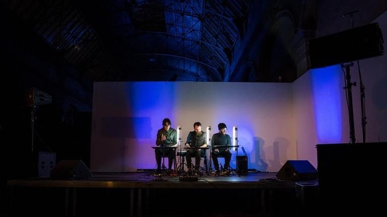 Drei Männer mit Neonlichtern auf der Bühne