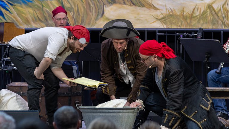 Drei Schauspieler mit Musikern im Hintergrund beim Live-Kinderhörspiel "Seeräuber-Moses"