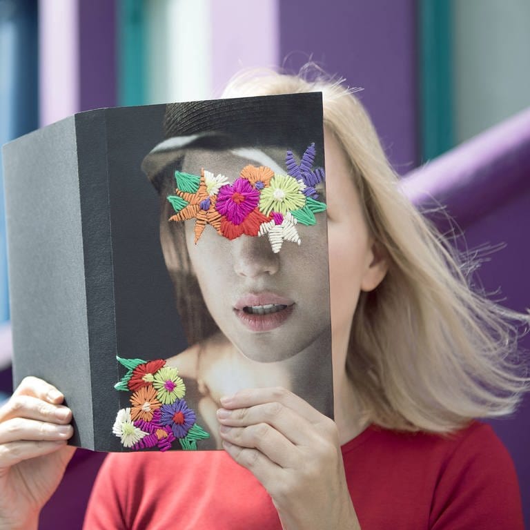 Frau bedeckt ihr Gesicht mit einem Buch (Foto: IMAGO, imago / Westend61)