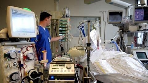 In einem Zimmer auf der Intensivstation bedient ein Mediziner eine Maschine zur Versorgung eines Patienten