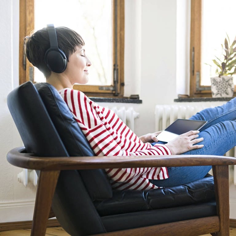 Frau mit aufgesetzten Kopfhörern in einem Sessel