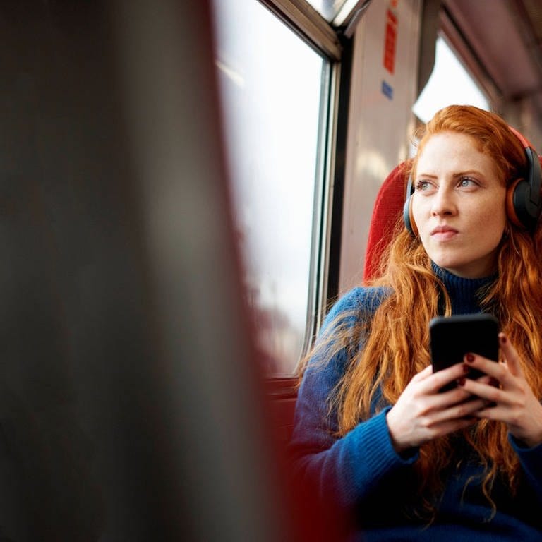 Eine Frau mit Kopfhörern während einer Bahnfahrt 