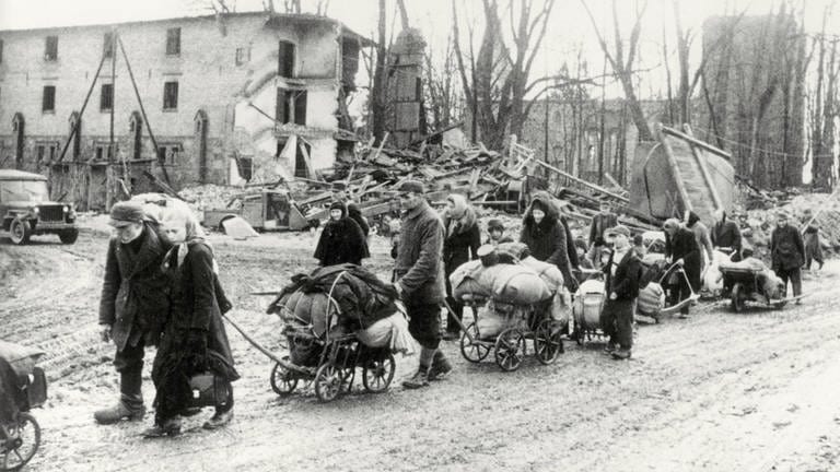 Flucht aus den deutschen Ostgebieten vor den vorrückenden Truppen der Roten Armee im Frühjahr 1945: eine Gruppe von Flüchtlingen mit Handwagen in einer zerstörten Ortschaft in Ostpreußen