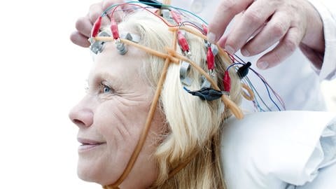 Einer Frau werden Sacht die Elektroden eines EEG am Kopf angebracht