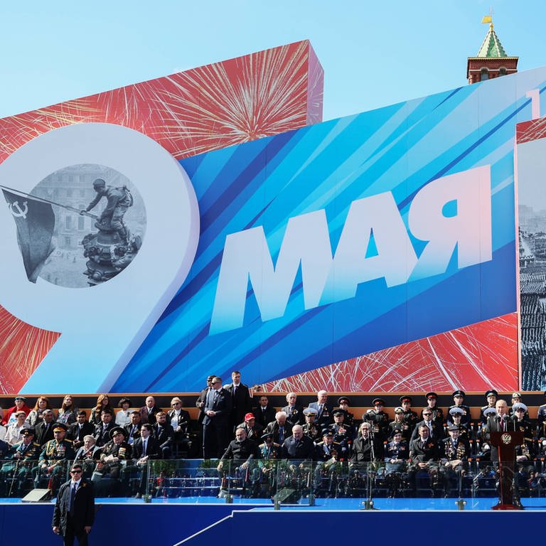 Wladimir Putin hält am "Tag der Befreiung", dem 9. Mai 2023, eine Rede in Moskau. Hinter ihm eine riesige Plakatwand, auf der u. a. zu lesen ist "1945 - 2023". Ganz links auf der Wand ist das ikonische Foto zu sehen, auf dem sowjetische Soldaten im Mai 1945 die rote Flagge auf dem Berliner Reichstag installieren und damit den Sieg über Nazi-Deutschland feiern. Im russischen Angriffskrieg gegen die Ukraine setzen beide Parteien immer wieder auf Propaganda – auch die Ukraine.