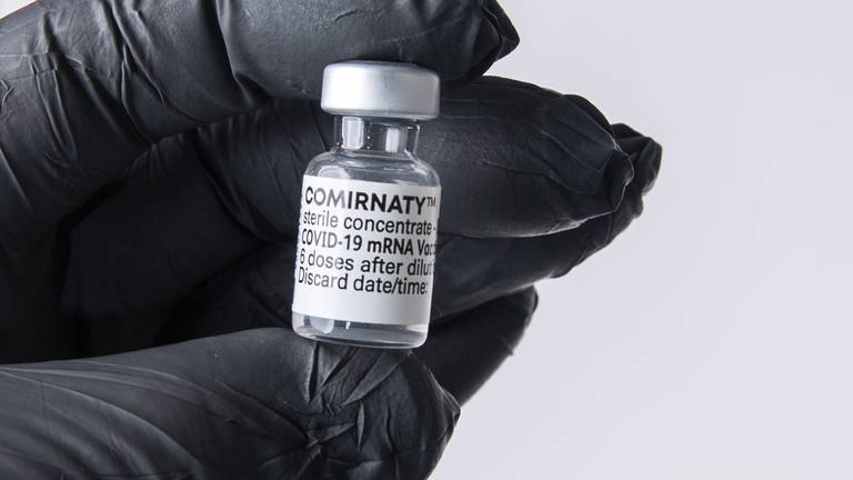 Eine Person mit Schutzhandschuh hat eine Ampulle mit dem mRNA-Impfstoff Comirnaty.