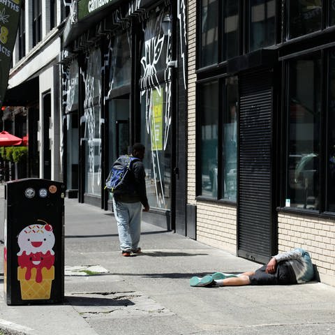 Mann liegt auf dem Fußweg ein Zweiter dreht sich nach ihm um, Ecke SW Broadway- SW Ankeny St, Downtown der Stadt Portland (Foto: IMAGO, IMAGO / Andreas Beil)
