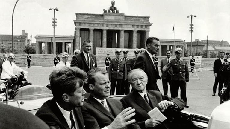 Präsident John F. Kennedy (links), Willy Brandt (Mitte; Bürgermeister von West-Berlin) und Bundeskanzler Konrad Adenauer am 26. Juni 1963 in einem Auto am Brandenburger Tor