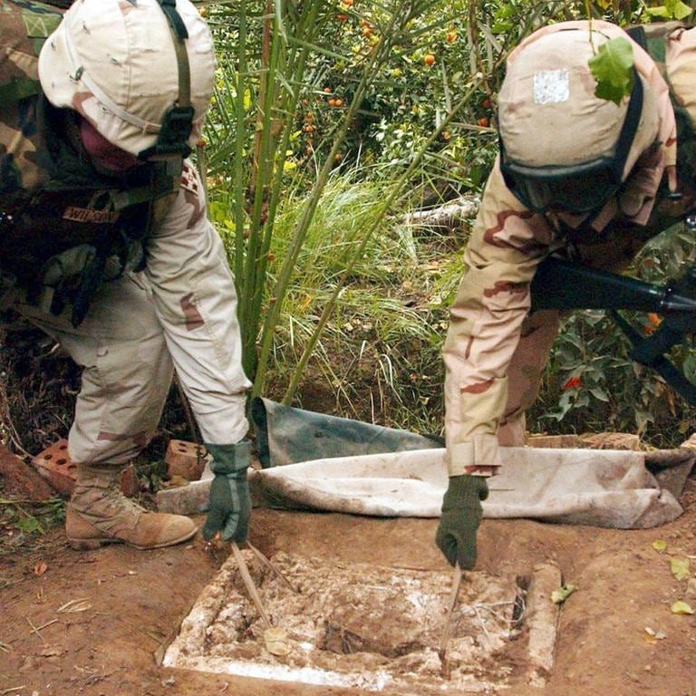Zwei US-Soldaten der 1. Brigade der 4. Infanteriedivision heben die Schaumstoffabdeckung auf das Erdloch, in dem sich der ehemalige irakische Führer Saddam Hussein versteckt gehalten hatte. Spezialeinheiten nahmen Hussein am 15. Dezembr 2003 hier fest.