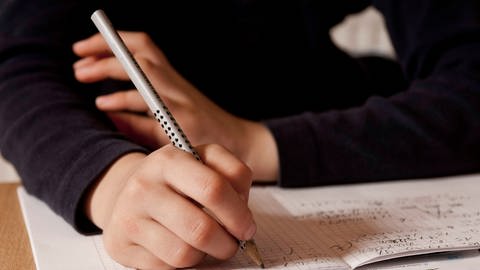 Grundschüler schreibt mit einem Bleistift ins Heft