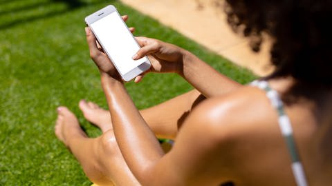 Eine Frau sitzt mit einem Handy in der Sonne